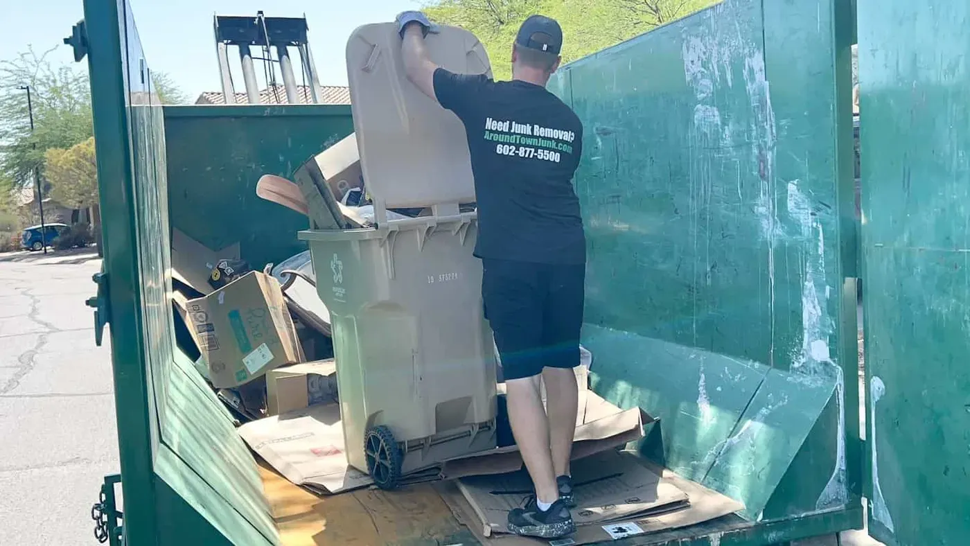 A crew member emptying an overflowing bin into a roll-off dumpster